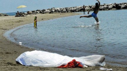 Des touristes continuent de jouer sur la plage alors que le corps d'une femme recouvert d'un drap blanc attend d'&ecirc;tre enlev&eacute;, Formia (Italie), le 17 juin 2013. (MAXPPP)