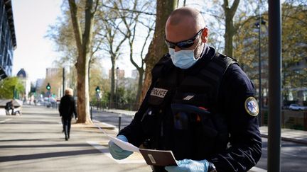 Un policier vérifie l'attestation et le passeport d'un citoyen dans les rues de Toulouse (Haute-Garonne), le 27 mars 2020. (ALAIN PITTON / AFP)