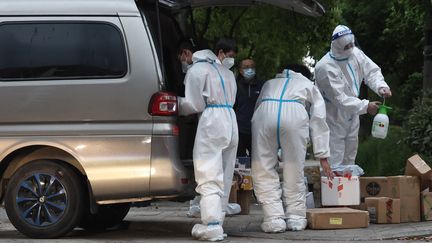 Des ouvriers déchargent et désinfectent des colis à la porte d'une communauté du district de Jiading, à Shanghai, le 25 avril 2022.&nbsp; (CHEN JIANLI / XINHUA)