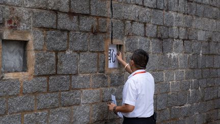 Un agent de sécurité enlève des morceaux de papier imprimés du caractère chinois "honte" affichés à l'emplacement d'une sculpture marquant la répression&nbsp;de&nbsp;Tiananmen, après qu'elle ait été retirée de l'université Lingnan à Hong Kong, le 24 décembre 2021. (BERTHA WANG / AFP)