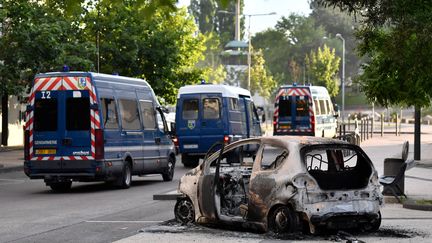 Des camions de gendarmerie passent devant un véhicule carbonisé après plusieurs jours de violences entre communautés à Dijon (PHILIPPE DESMAZES / AFP)