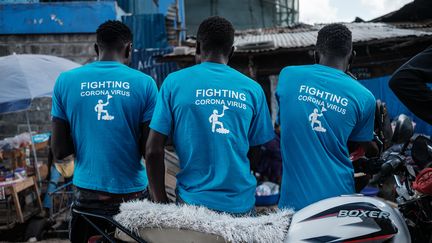 Dans le bidonville géant de Kibera à Nairobi (Kenya), trois membres d'une ONG locale portent des T-shirts avec le slogan "Combattre le coronavirus" devant un point de lavage des mains qu'ils ont inauguré. (YASUYOSHI CHIBA / AFP)