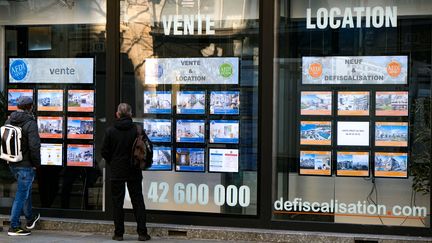 Deux passants scrutent les annonces pour des appartements à vendre dans la vitrine d'une agence immobilière. 28 01 2023. (NICOLAS GUYONNET / HANS LUCAS)