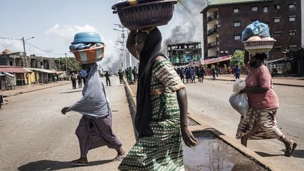 Des femmes traversent la route en courant, dans la capitale guinéenne Conakry, lors d'une manifestation de masse le&nbsp;lendemain de&nbsp;la publication des résultats préliminaires pour cinq communes de la ville, le 21 octobre 2020. (JOHN WESSELS / AFP)