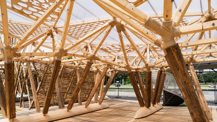 Baptisé "Les Ram'eaux", le pavillon réalisé par l'Ensa Nancy pour la Fédération française d'aviron est une structure en bois massif qui s'inspire de la gestuelle des rameurs. Elle "est portée par des poteaux reprenant la figure du skiff, embarcation emblématique de l'aviron", indique son descriptif. Au sol, des "lignes d'eau" délimitent "le parcours de déambulation". La conception du pavillon a été possible grâce à une modélisation numérique, qui a permis "la création de nœuds d'assemblage complexes", une singularité de la construction. (PAULINER GAUER / SIPA PRESS / MINISTERE DE LA CULTURE)