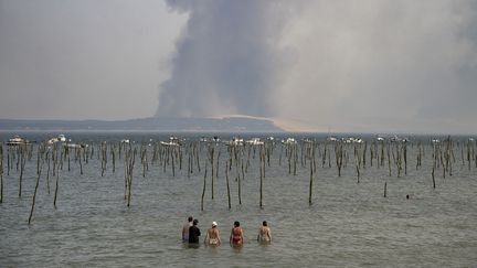 Des touristes regardent le panache de fumée sombre au-dessus de la dune du Pilat depuis le Cap Ferret en raison d'un incendie de forêt près de La Teste-de-Buch (Gironde), le 18 juillet 2022. (OLIVIER MORIN / AFP)