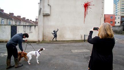 Des passants devant une œuvre de Banksy, à Bristol, le 14 février 2020. (GEOFF CADDICK / AFP)