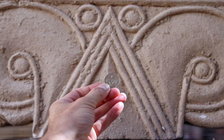 Une pièce de cinq shekels placée en face d'un chapiteau antique présenté en septembre 2020 à Jérusalem.&nbsp; (EMMANUEL DUNAND / AFP)