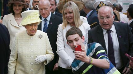 Un gar&ccedil;on se glisse devant Elizabeth II pour r&eacute;aliser un selfie,&nbsp;&agrave; Belfast (Irlande du Nord, Royaume-Uni), le 24 juin 2014. (PETER MACDIARMID / AFP)