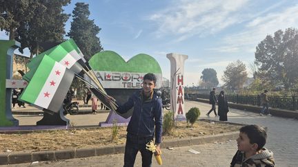 Un habitant de Hama brandit les drapeaux de la nouvelle Syrie, le 12 décembre 2024. (MARIE-PIERRE VEROT / RADIO FRANCE)