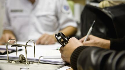 Un médecin&nbsp;accompagné d'un policier remplit un formulaire (illustration). (JAMES HARDY
 / MAXPPP)