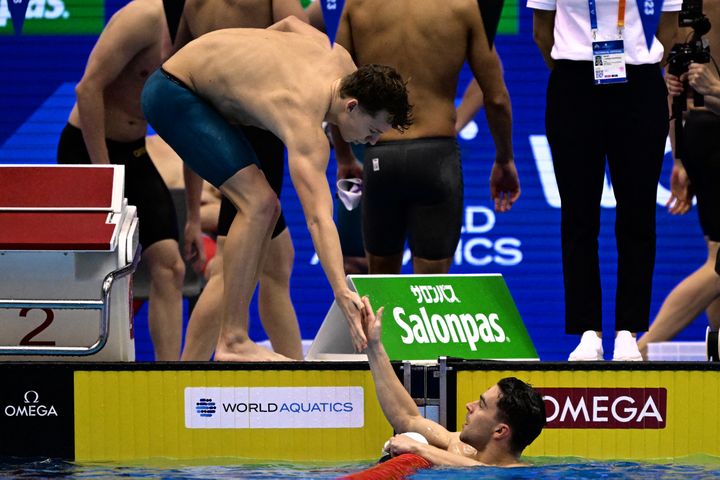 Le nageur français Léon Marchand frappe la main de son collègue du relais 4x100m quatre nages, Hadrien Salvan lors des séries des Mondiaux de natation de Fukuoka, le 30 juillet 2023 (YUICHI YAMAZAKI / AFP)