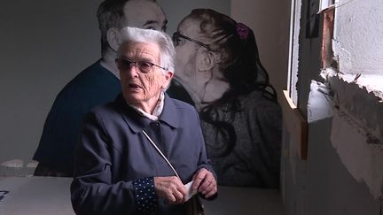 Madeleine Ameilbonne, une ancienne habitante de la Muraille est revenue dans les lieux : "Je voudrais un caillou, en souvenir".&nbsp;Derrière elle, une photo d'habitants signée Charles Rostan. (L. Pastural / France Télévisions)