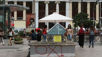 Des passants sur une place &agrave; Ath&egrave;nes, le 29 juin 2015, &agrave; proximit&eacute; d'un appel &agrave; voter "non" (Oxi) au r&eacute;f&eacute;rendum sur les conditions du plan d'aide &agrave; la Gr&egrave;ce, dimanche 5 juillet, inscrit sur un banc. (AYHAN MEHMET / ANADOLU AGENCY/AFP)