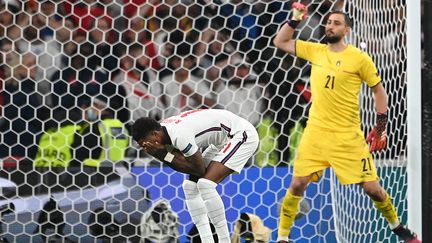 Marcus Rashford se tient le visage en détresse après avoir envoyé son tir au but sur le poteau gauche de Gianluigi Donnarumma. Ce&nbsp;raté était le premier d’une série de trois échecs consécutifs qui a offert le titre européen à l’Italie. Derrière, le portier Italien laisse échapper sa joie, lui qui arrêtera les deux prochains tirs au but anglais et sera élu meilleur joueur de la compétition par la suite.&nbsp; (ANDY RAIN / AFP)