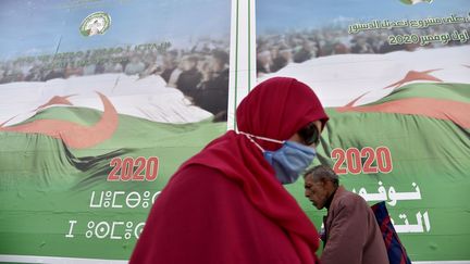 Deux passants devant les panneaux d'affichage de la campagne en vue du référendum sur la révision de la Constitution, le 22 octobre 2020 à Alger. (RYAD KRAMDI / AFP)