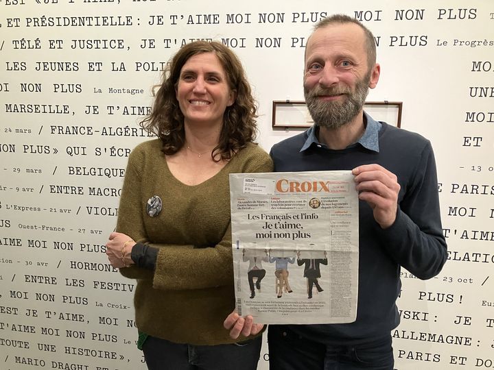 Caroline Raynaud et Sébastien Merlet, commissaires de l'exposition "Serge Gainsbourg, le mot exact",  à la La Bibliothèque publique d’information du entre Pompidou, le 25 janvier 2023, posent devant le mur qui recence les citations dans la presse de la chanson "Je t'aime moi non plus", avec entre les mains le journal Lacroix du jour, qui utilise une fois de plus ce titre (LAURENCE HOUOT / FRANCEINFO CULTURE)