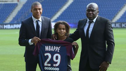 Kylian Mbappé lors de sa présentation officielle en tant que joueur du Paris Saint-Germain, avec son petit frère Ethan et son père, le 6 septembre 2017. Le maillot porte le numéro 29, en hommage à la date de naissance d'Ethan, né le 29.  Décembre 2006. (ALFONSO JIMENEZ / SIPA)