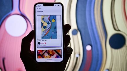 Un visiteur tenant un téléphone portable affichant une œuvre d'art virtuelle vendue&nbsp;lors de&nbsp;l'Art Basel, la première foire d'art moderne et contemporain au monde, le 14 juin 2022 à Bâle. (SEBASTIEN BOZON / AFP)