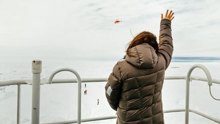 Une passag&egrave;re du navire russe pi&eacute;g&eacute; dans les glaces de l'Antarctique salue l'h&eacute;licopt&egrave;re du brise-glaces chinois venu les secourir,&nbsp;le 29 d&eacute;cembre 2013. (ANDREW PEACOCK / FOOTLOOSEFOTOGRAPHY.COM / AFP)