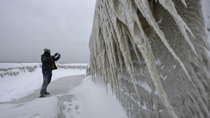 Un homme photographie les stalactites géantes qui se sont formées sur cette maison du comté de Buffalo (New York), en raison des vents glaciaux, le 26 décembre 2022. (FATIH AKTAS / ANADOLU AGENCY / AFP)