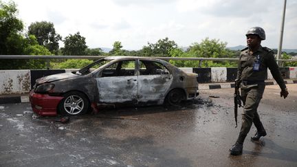 Un policier passe devant une voiture incendiée par des partisans d'Ibrahim Zakzaky, un dirigeant emprisonné du Mouvement islamique du Nigeria (MIN), près du bâtiment de l'Assemblée nationale à Abuja, la capitale du Nigeria, le 9 juillet 2019. (KOLA SULAIMON / AFP)