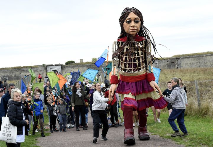 Amal, la marionnette géante représentant une fillette réfugiée syrienne, avance&nbsp;sur une route de Calais (France) pour le projet international "The Walk", le 17 octobre 2021, avant de gagner la Grande-Bretagne.&nbsp; (FRANCOIS LO PRESTI / AFP)