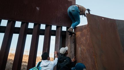 Des migrants sud-américains escaladent un mur à la frontière entre les États-Unis et le Mexique.&nbsp; (ARIANA DREHSLER / MAXPPP)
