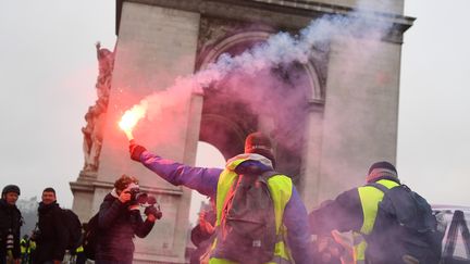 Un homme en "gilet jaune" brandit un fumigène devant l'Arc de Triomphe. (ALAIN JOCARD / AFP)