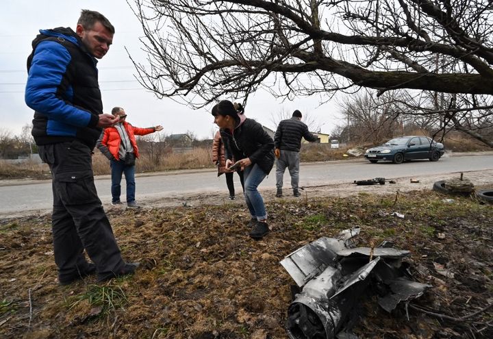 Des habitants&nbsp;prennent des photos des restes d'une roquette dans une zone résidentielle de Kiev, le 25 février 2022. (GENYA SAVILOV / AFP)