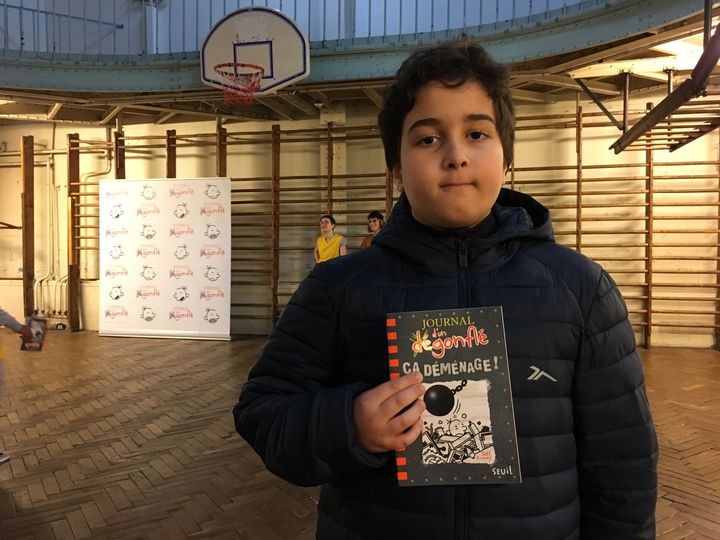 Younes, 11 ans,&nbsp;élève du collège Georges Rouault (Paris 19e) pose avec Le Jounal d'un dégonflé - Ca déménage !" (Seuil Jeunesse), le 10 décembre 2019 (Laurence Houot / franceinfo Culture)