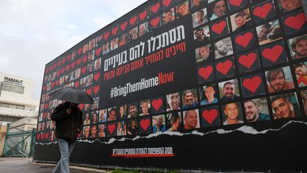 Un homme marche devant un mur sur lequel est installé un grand poster des otages israéliens détenus par le Hamas, le 2 février 2024 à Jérusalem. (AHMAD GHARABLI / AFP)