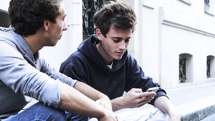 Des adolescents consultent leurs portables, &agrave; Paris, le 5 ao&ucirc;t 2015. (NATHAN ALLIARD / PHOTONONSTOP/AFP)