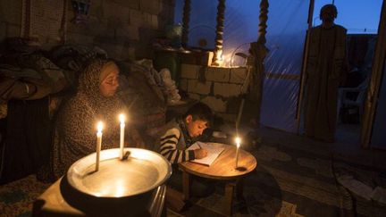 Une Palestinienne aide son fils à faire ses devoirs à la lueur de bougies, dans leur maison à Khan Younès, dans le sud de la Bande de Gaza, le 19 avril 2017. (MAHMUD HAMS / AFP)