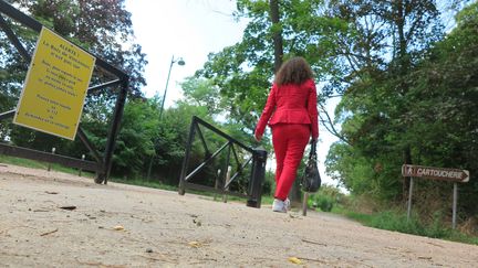 A woman walks past a sign warning of the presence of a sexual predator in the Bois de Vincennes, in Paris, on August 7, 2024. (FLORIAN LOISY / LE PARISIEN / MAXPPP)