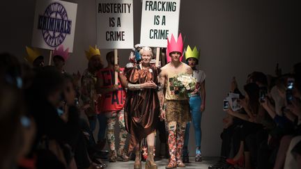 Fidèle à elle-même et à son engagement écologique, la Britannique Vivienne Westwood a transformé la Fashion Week de Londres en tribune politique. Coutumière des happenings, la créatrice rebelle de 74 ans avait donné rendez-vous dans un sous-sol de l'Université de Westminster pour la présentation de sa ligne Red Label. Extinction des lumières, hurlements de sirènes... des projecteurs s'allument, braqués sur un groupe brandissant des pancartes "L'austérité est un crime" ou "La fracturation hydraulique est un crime", en référence à la technique permettant d'extraire du gaz de schiste."Les politiciens font peser sur nous un incroyable danger et nous devons les arrêter. Ils provoquent la guerre et le changement climatique", a expliqué l'ancienne égérie du mouvement punk dans une lettre. L'attaque semble viser le Premier ministre conservateur David Cameron qu'elle avait interpellé la semaine dernière sur le thème de la fracturation hydraulique en chevauchant un char jusque devant son domicile à la campagne.  
 (LEON NEAL / AFP)