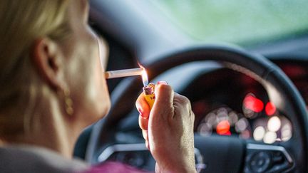 Une femme s'allume une cigarette en voiture. (AXEL HEIMKEN / DPA)