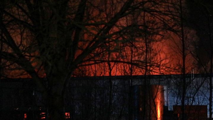 Le ciel orangé par les flammes de l'incendie survenu dans un bâtiment industriel loué par Bolloré Logistics, à Grand-Couronne, près de Rouen (Seine-Maritime), le 16 janvier 2023. (LOU BENOIST / AFP)