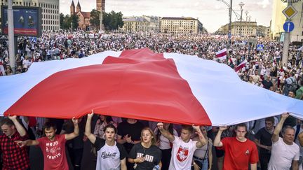 Sous un drapeau blanc et rouge qui est le signe de ralliement des opposants, une manifestation géante conteste la réélection d'Alexandre Loukachenko à la tête de la Biélorussie, &nbsp;le 16 août 2020 à Minsk. (SERGEI GAPON / AFP)