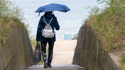 Une touriste se dirige vers la plage avec un parapluie, le 22 juillet 2023, à Zinnowitz (Allemagne). (STEFAN SAUER / DPA / AFP)