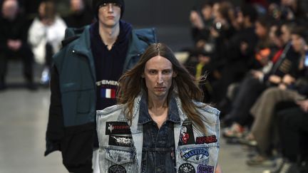 Vetements, qui présentait son prêt-à-porter hiver 2017, célébre les cultures populaires, le kitsch et le quotidien. Demna Gvasalia fait défiler une Parisienne en trench-coat beige et jean slim. Pour la secrétaire, un tailleur-jupe, un chemisier décolleté. Le hooligan est vêtu d'un bomber XXL, un pantalon de survêtement et une écharpe de foot aux couleurs criardes, le vagabond a un pull en laine effiloché aux couleurs du drapeau européen, un grand manteau qui se ferme à l'aide d'une écharpe et un sac de couchage siglé Vetements. Une grand-mère est habillée d'une ample parka, un chemisier en soie dans une jupe plissée couleur anis.
 (ALAIN JOCARD / AFP)