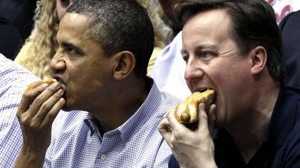 Le pr&eacute;sident am&eacute;ricain Barack Obama (G) et le Premier ministre britannique David Cameron d&eacute;vorent un hot-dog devant un match de basket en Ohio, le 13 mars 2012. (LARRY DOWNING / REUTERS)