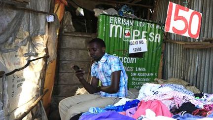 Un commerçant attend les clients dans sa boutique de textiles de seconde main à Nairobi. Le sigle M-Pesa, que l'on voit sur une affiche derrière lui, est un système de paiement par l'intermédiaire d'un téléphone mobile.  ( REUTERS - Noor Khamis)