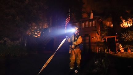 Un pompier enroule un tuyau devant une maison, le 21 août 2020, à Boulder Creek (Californie). (MARCIO JOSE SANCHEZ/AP/SIPA)