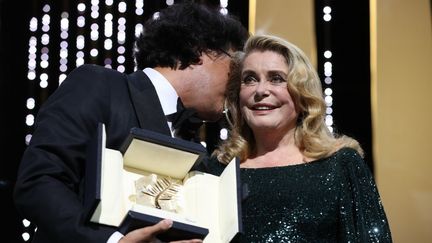 Le réalisateur Bong Joon-Ho chuchote à l'oreille de Catherine Deneuve après qu'elle lui ait remis sa Palme d'Or pour&nbsp;Parasite (VALERY HACHE / AFP)