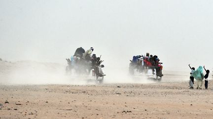 Une femme et ses enfants saluent des migrants assis sur des pick-up, alors qu'ils quittent la périphérie d'Agadez pour la Libye, d'où ils tenteront d'atteindre l'Europe. Le 1er juin 2015. (ISSOUF SANOGO / AFP)