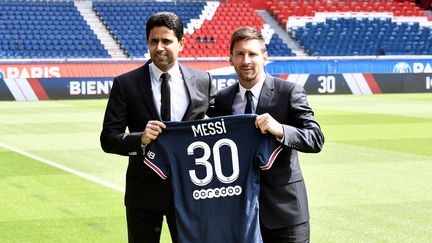 Lionel Messi présente son maillot du PSG floqué du numéro 30, aux côtés du président du club, Nasser Al-Khelaifi, sur la pelouse du Parc des Princes le 11 août 2021. (STEPHANE DE SAKUTIN / AFP)