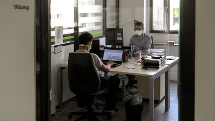 Deux salariés, avec masques et séparés par du plexiglas, dans une entreprise de&nbsp;Venissieux, près de Lyon, en aout 2020. (MAXIME JEGAT / MAXPPP)