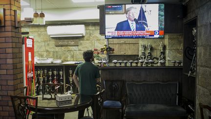 Un homme regarde à la télévision Donald Trump annoncer la sortie des Etats-Unis des accords sur le nucléaire iranien, dans le centre de Téhéran, le 8 mai 2018. (AHMAD HALABSIAZ / XINHUA)