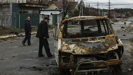 Des passsants&nbsp;près d'une voiture&nbsp;détruite à&nbsp;Boutcha,&nbsp;près d'Irpin, dans la banlieue de Kiev (Ukraine), le 2&nbsp;avril 2022. (RONALDO SCHEMIDT / AFP)